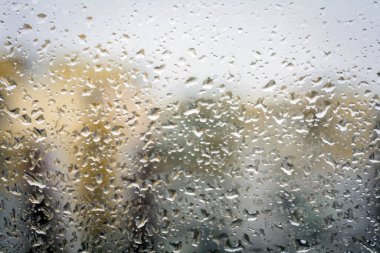 Camdaki yağmur damlaları, dışardaki binaların pencere arkaplan görüntüsü