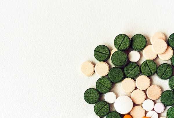 Лекарства зеленые, розовые и желтые таблетки или капсулы на белом спине

