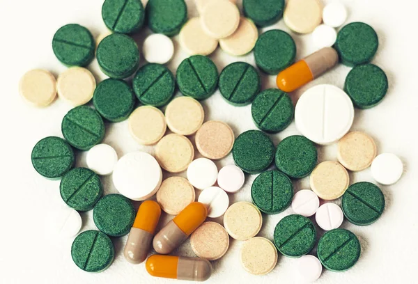 Лекарства зеленые, розовые и желтые таблетки или капсулы на белом спине — стоковое фото