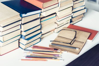 Not defteri, kalemler, gözlük ve kitap yığını, okul geçmişi.