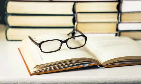 Libros de fondo, libro abierto y vasos sobre mesa de madera blanca en — Foto de Stock