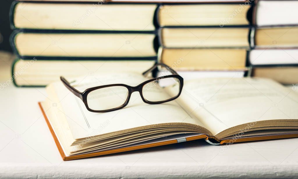 Books background, open book and glasses on white wooden table in
