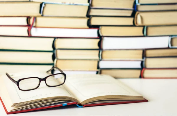 Libros de fondo, libro abierto y vasos sobre mesa de madera blanca en — Foto de Stock