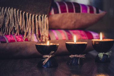 Hindistan cevizi kabuğu ve bordo yastıklarla yanan spa aromalı mumlar.