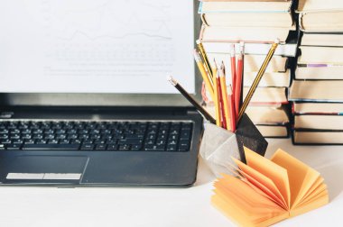 Dizüstü bilgisayar, kitap yığını, defter, ofis arka planında kalemler...