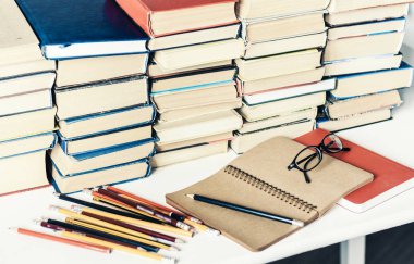 Yığınla eski kitap, ders kitabı, defter, gözlük ve kalem.