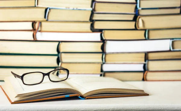 Libros de fondo, libro abierto y vasos sobre mesa de madera blanca en — Foto de Stock