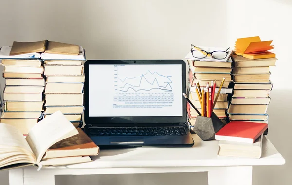 Laptop, stack of books, notebook, pencils in office background f