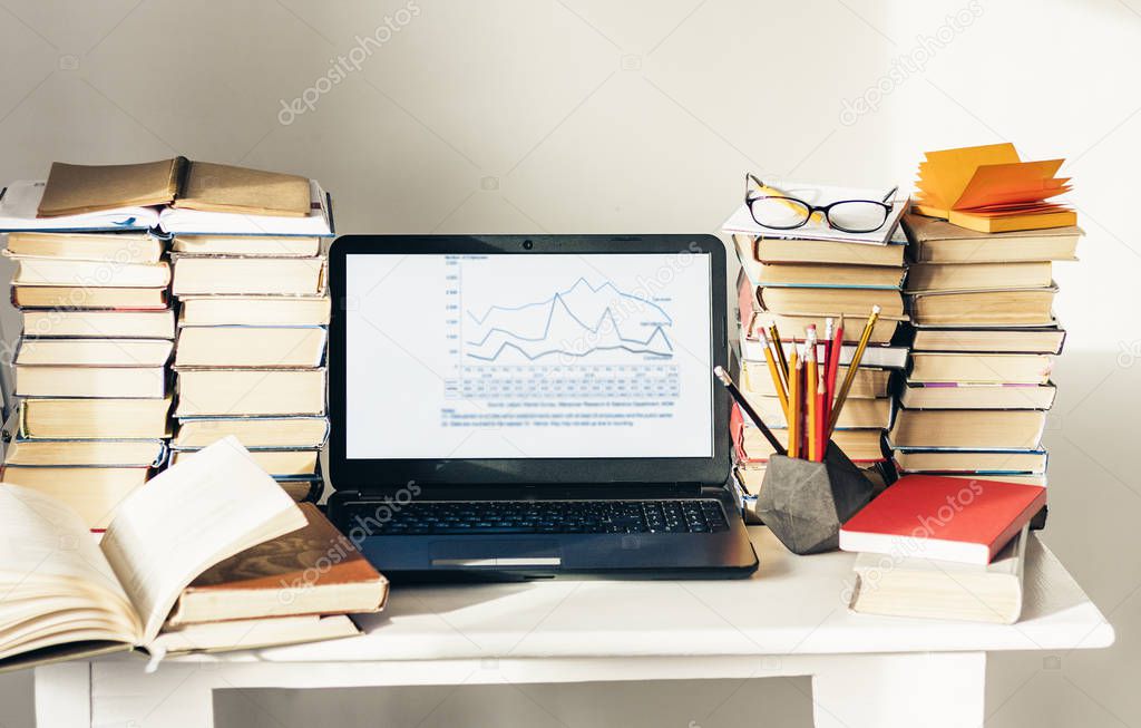 Laptop, stack of books, notebook, pencils in office background f