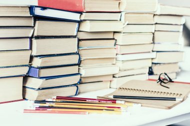 Yığınla eski kitap, ders kitabı, defter, gözlük ve kalem.