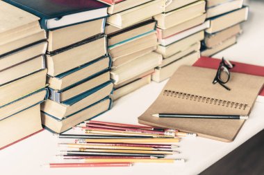 Yığınla eski kitap, ders kitabı, defter, gözlük ve kalem.