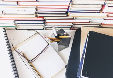 Dizüstü bilgisayar, kitap yığını, defter, ofis arka planında kalemler...