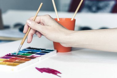 Kadın eli, bir fırça ve bir çarşafa suluboya boya çizer.