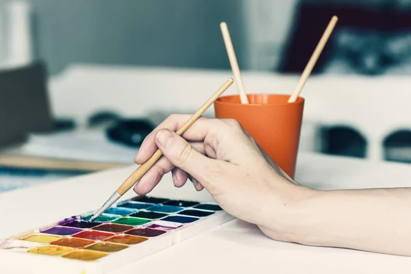 Main féminine dessine avec un pinceau et peinture à l'aquarelle sur une feuille o — Photo