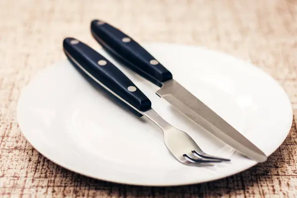 Piatto bianco vuoto con coltello e forchetta su fondo legno  . — Foto Stock