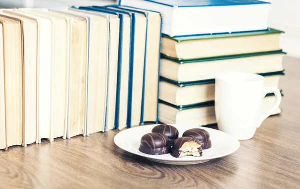Stack of books, cup of coffee and chocolate cookies white plate. Stock Picture