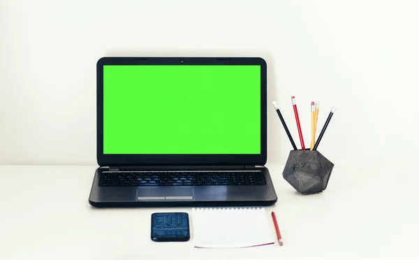 Green screen laptop, smartphone, notebook and pencils in concret