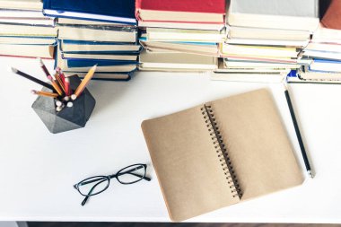 Yığınla eski kitap, ders kitabı, defter, gözlük ve kalem.