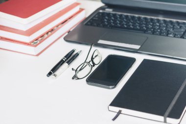 Laptop, akıllı telefon, yığınla kitap, kalem, gözlük, defter.