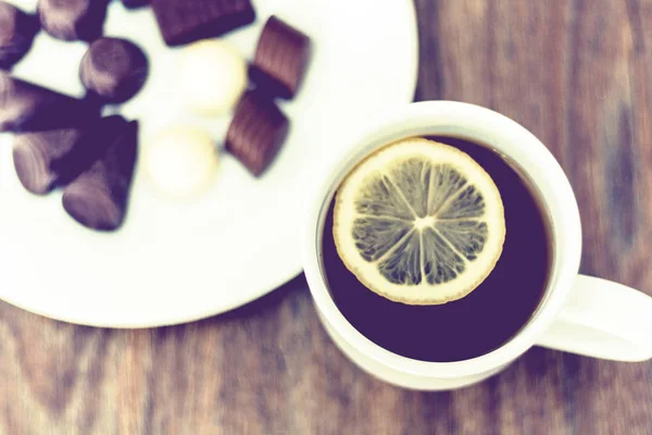 Caramelos de chocolate en plato blanco y taza de té con limón . — Foto de Stock