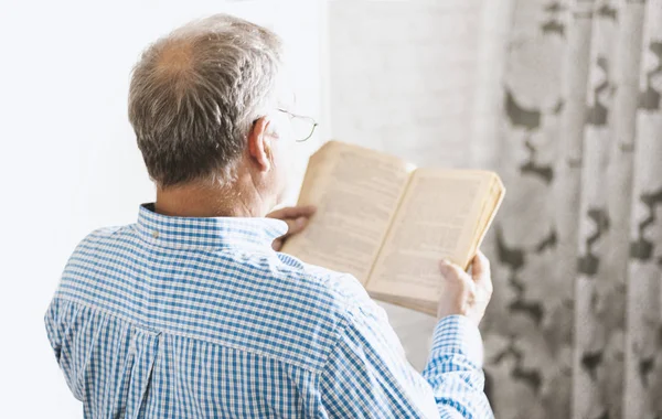 Orta yaşlı, gri gözlüklü, mavi gömlekli, kitap okuyan bir adam. 