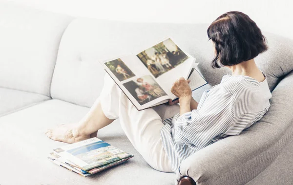Mujer morena de mediana edad en el sofá gris mirando el ingenio del álbum — Foto de Stock