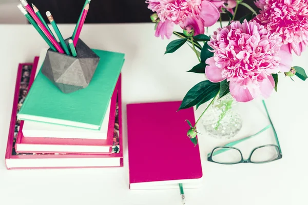 Boeket van roze pioenen, een stapel boeken, potloden en een noteboo — Stockfoto