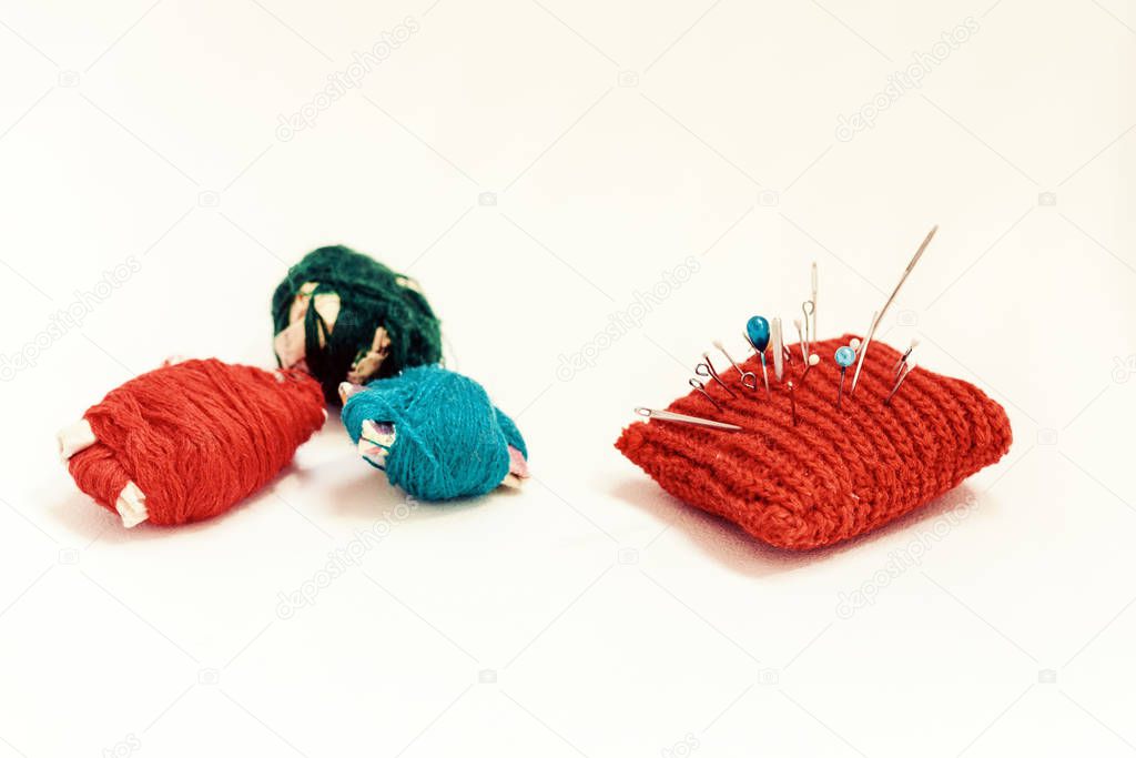Red knitted needle pad for sewing and colored thread coils on wh