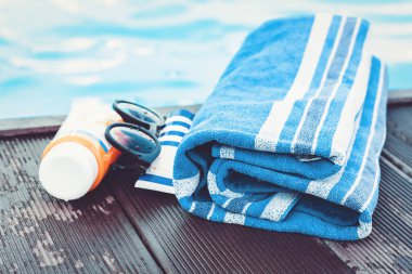 Güneş gözlüğü, güneş kremi tüpü, mavi havlu, yüzmeye yakın. 