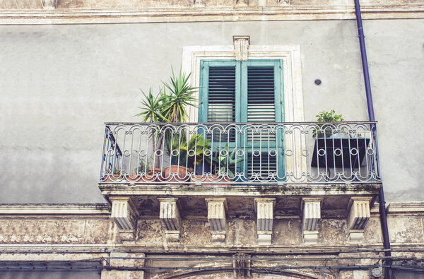 Balcony with flowerpots and house palm plants in a historic building in Catania, traditional architecture of Sicily, Italy