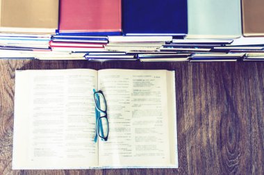 Kitap arkaplanı, açık kitap ve gözlükler ofisteki ahşap masada.