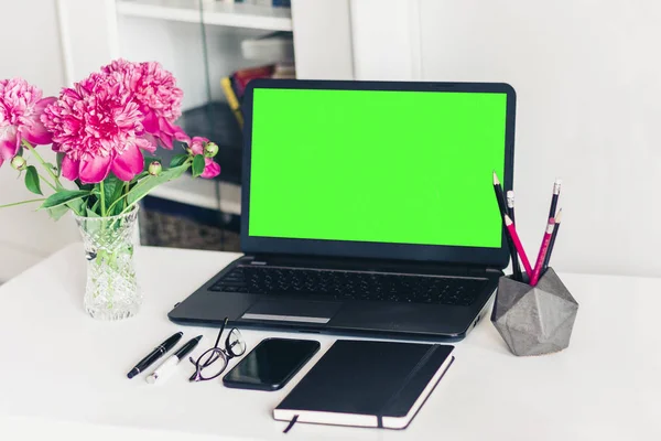 Buquê de peônias rosa, laptop de tela verde, smartphone, canetas , — Fotografia de Stock