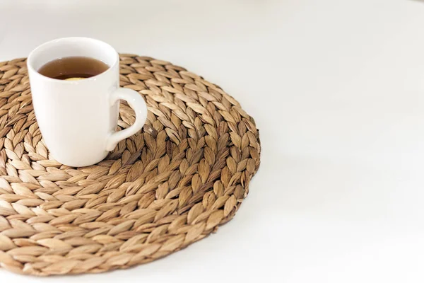 Lemon tea in a white ceramic cup on a straw wicker stand on the — Stock Photo, Image