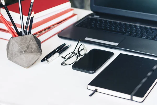 Stapel boeken, smartphone, laptop, bril en potloden in houder — Stockfoto