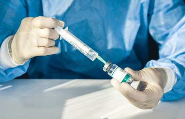 Doktor mavi ameliyat elbisesi ve maskesi ile elinde bir medikal tutuyor.