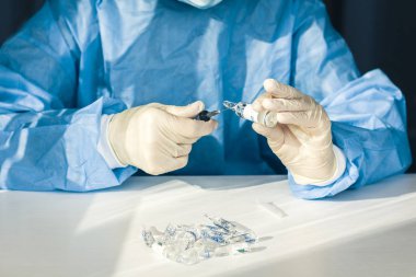 Doktor mavi ameliyat elbisesi ve maskesi ile elinde bir medikal tutuyor.