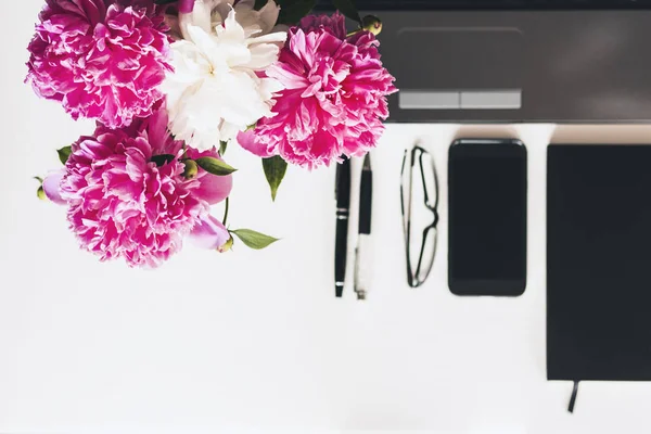 Buquê de peônias rosa, laptop, smartphone, canetas, óculos e um — Fotografia de Stock