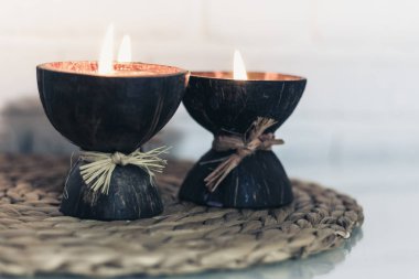 Hindistan cevizi kabuğunda yanan spa aromalı mumlar hasır tezgahta duruyor. 