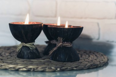 Hindistan cevizi kabuğunda yanan spa aromalı mumlar hasır tezgahta duruyor. 