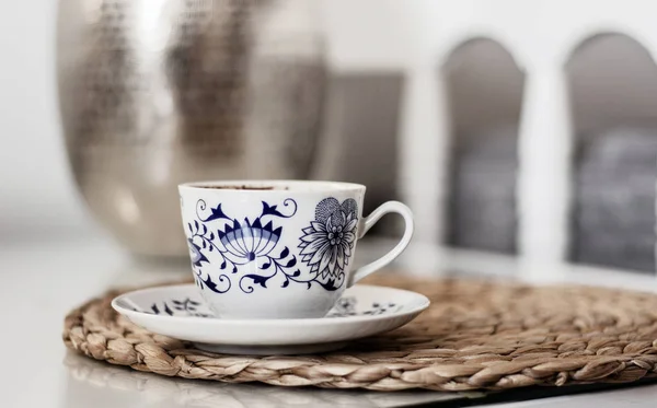 Kopje koffie op rieten onderstel op een glazen witte tafel, metalen vaas — Stockfoto