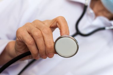 Kapalı el doktoru mavi tıbbi maskeli kadın stetoları gösteriyor.