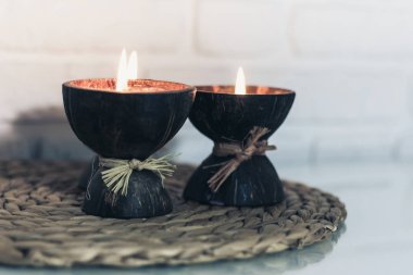 Hindistan cevizi kabuğunda yanan spa aromalı mumlar hasır tezgahta duruyor. 