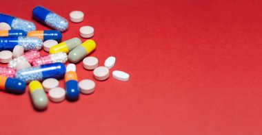 Kırmızı arka planda yığınla hap, tablet, kapsül. Uyuşturucu öncülü