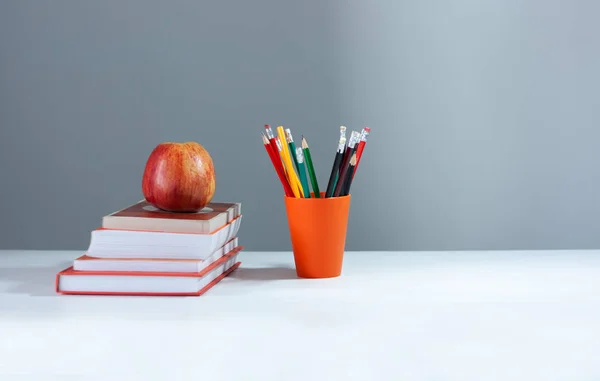 Porte-crayon orange, pile de livres sur table blanche avec application rouge — Photo