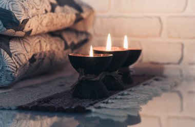 Hindistan cevizi kabuğunda yanan spa aromalı mum örülmüş çok renkli bir halı ve beyaz duvarın karşısındaki gri yastıklar, rahat ev içi.