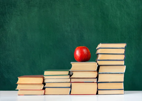 Back to school, pile of books and red apple with empty green school board background, education concept