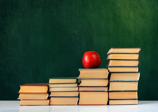 Okula, bir yığın kitap ve boş yeşil okul yönetim kurulu geçmişi olan kırmızı elma, eğitim kavramı.