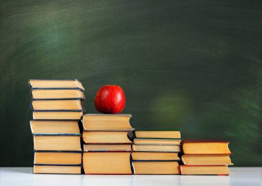 Okula, bir yığın kitap ve boş yeşil okul yönetim kurulu geçmişi olan kırmızı elma, eğitim kavramı.