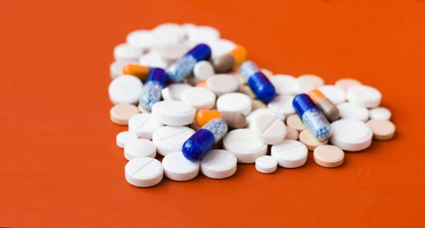 白い錠剤のヒープ 心臓の形をした錠剤 赤いオレンジの背景にカプセル 治療薬の処方コピースペースとヘルスケアの概念 — ストック写真