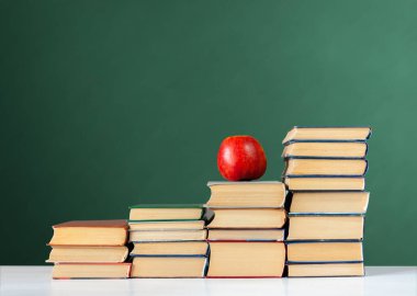 Okula, bir yığın kitap ve boş yeşil okul yönetim kurulu geçmişi olan kırmızı elma, eğitim kavramı.